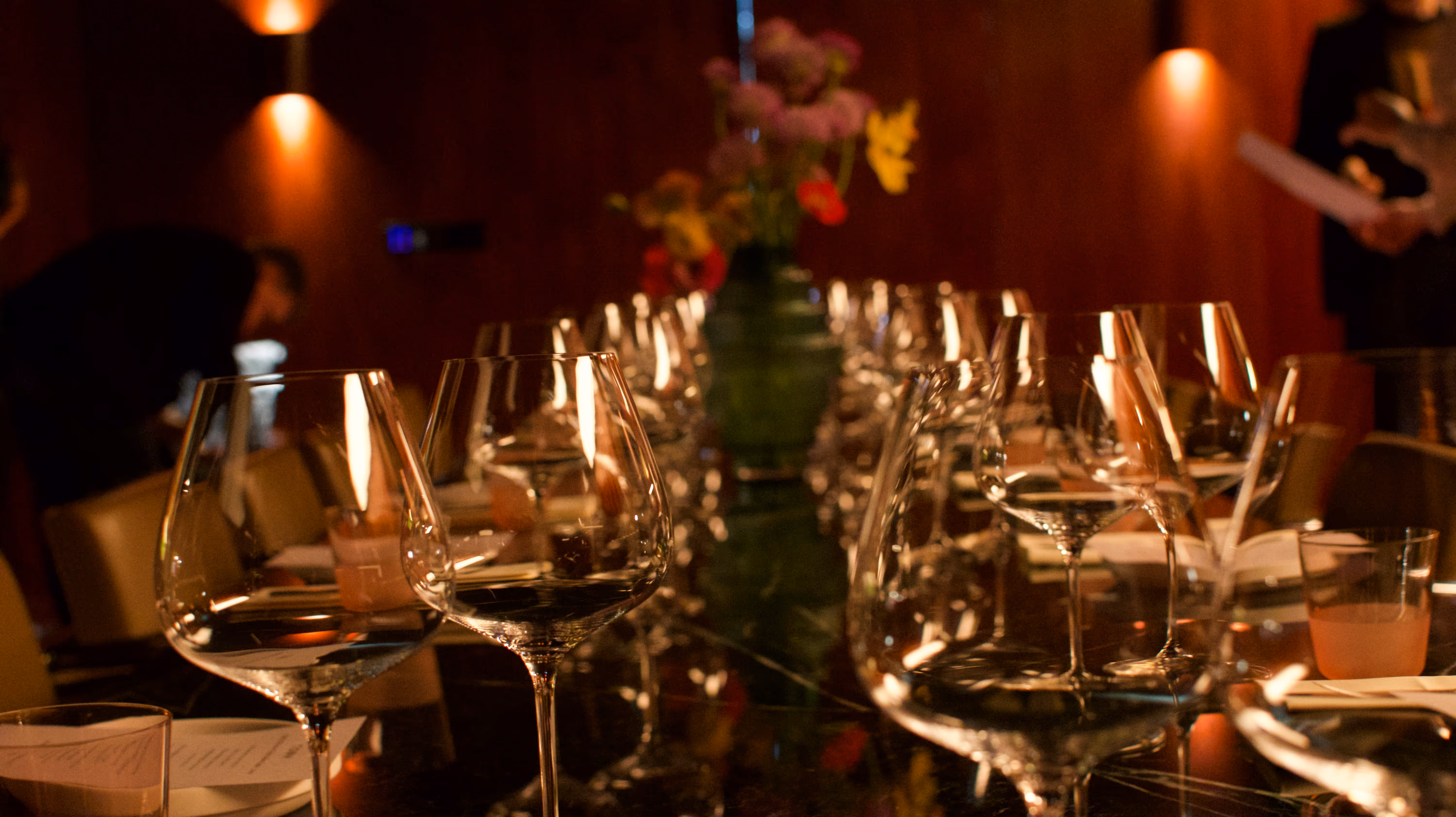 Long dining table with empty wine glasses and a flower vase in a dimly lit room.
