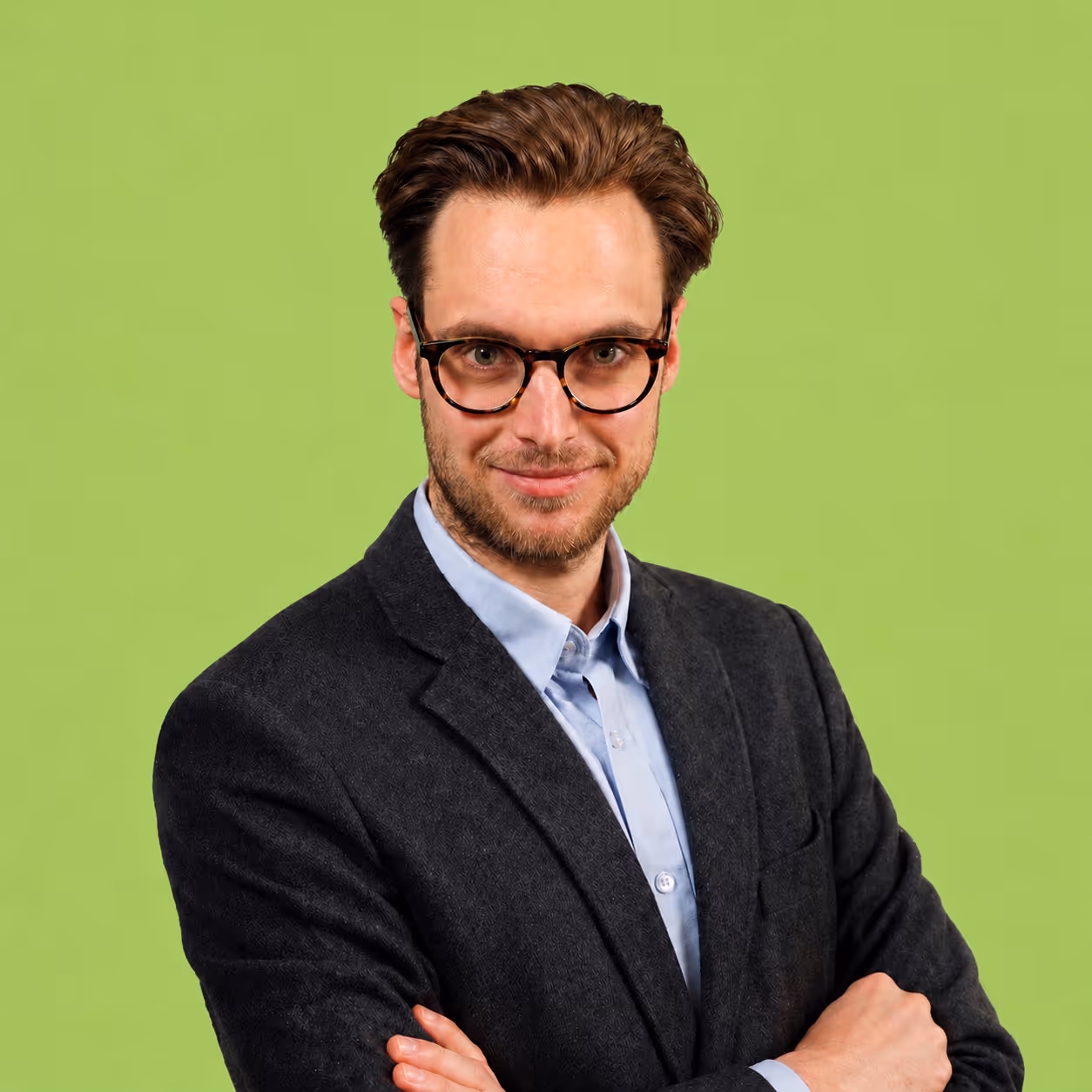 Mattia Scarpazza. Man with glasses wearing a dark blazer and blue shirt against beige background.