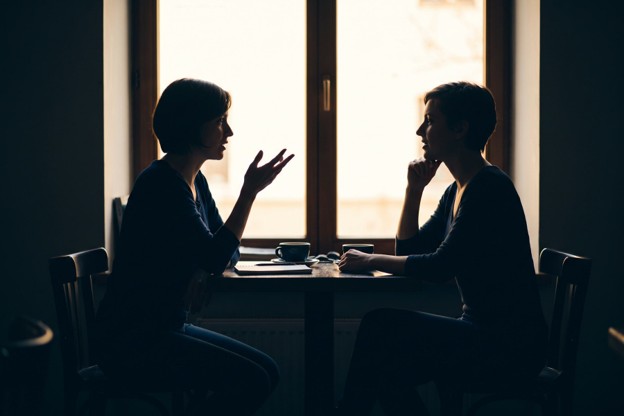 Two silhouetted figures sitting across from one another at a table.