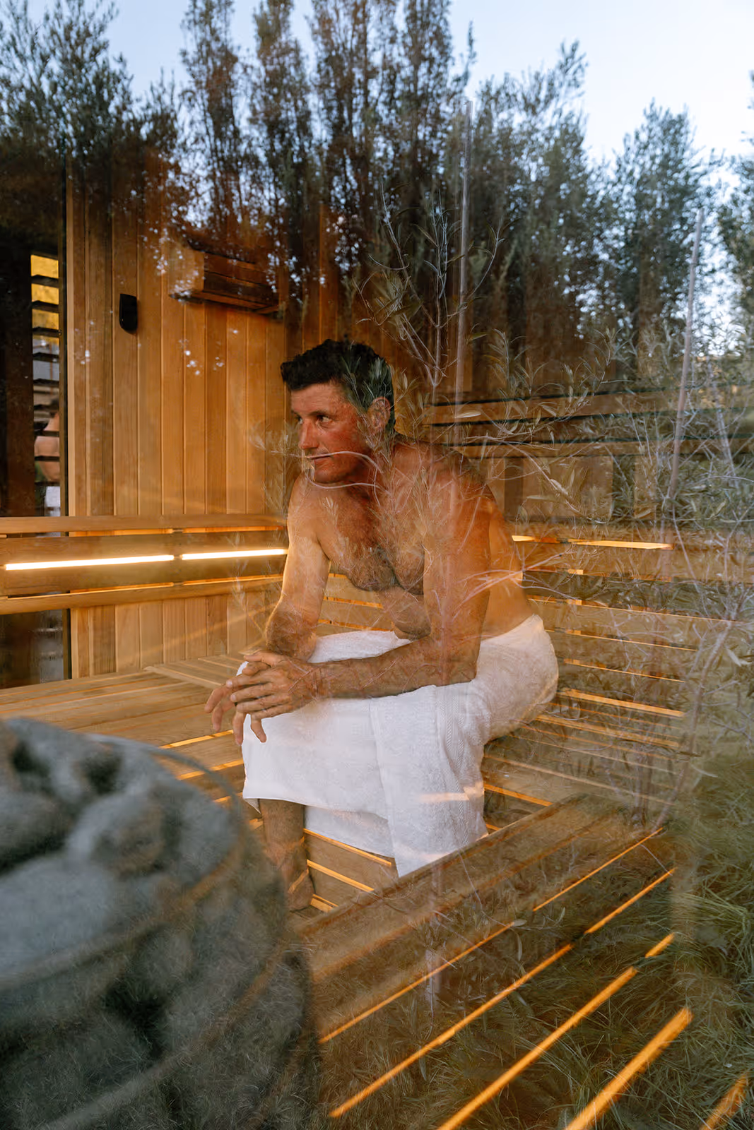 Looking through the glass of a sauna at a man sitting inside on the bench