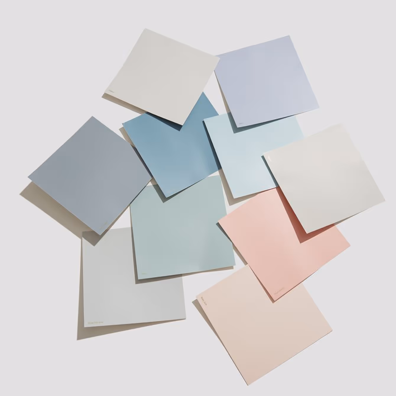 Array of nine paint color swatches in soft pastel shades of blue, pink, green, and beige arranged on a light surface.