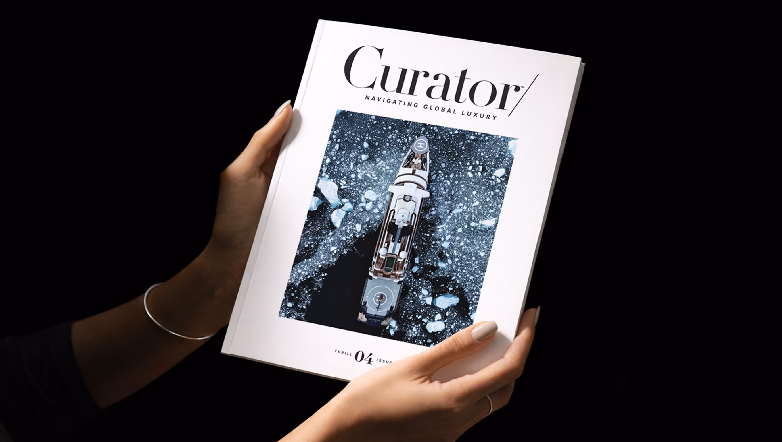 Hands holding the Curator magazine with a cover image of a yacht navigating icy waters.