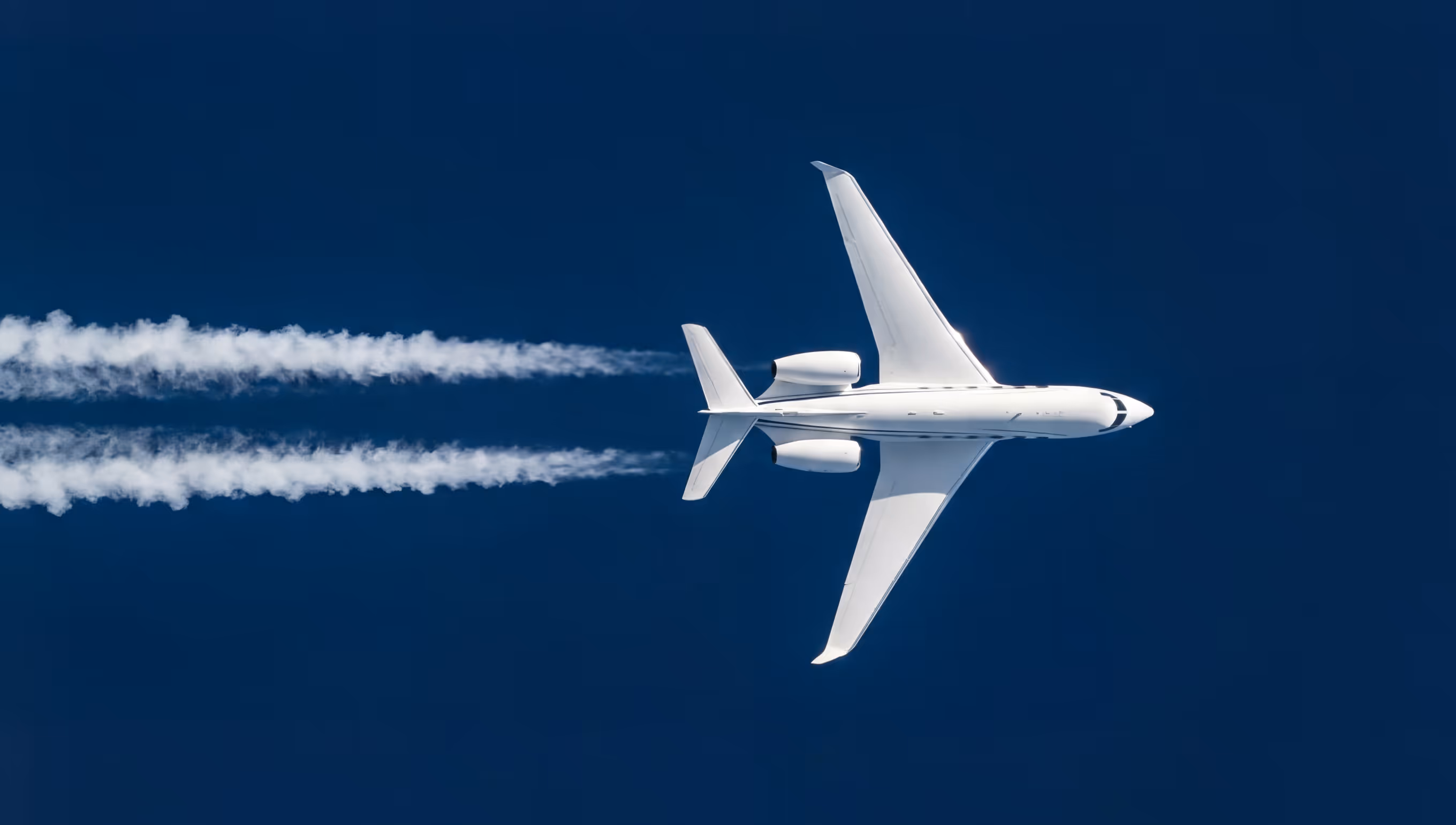 White airplane flying against a deep blue sky leaving behind two contrails.
