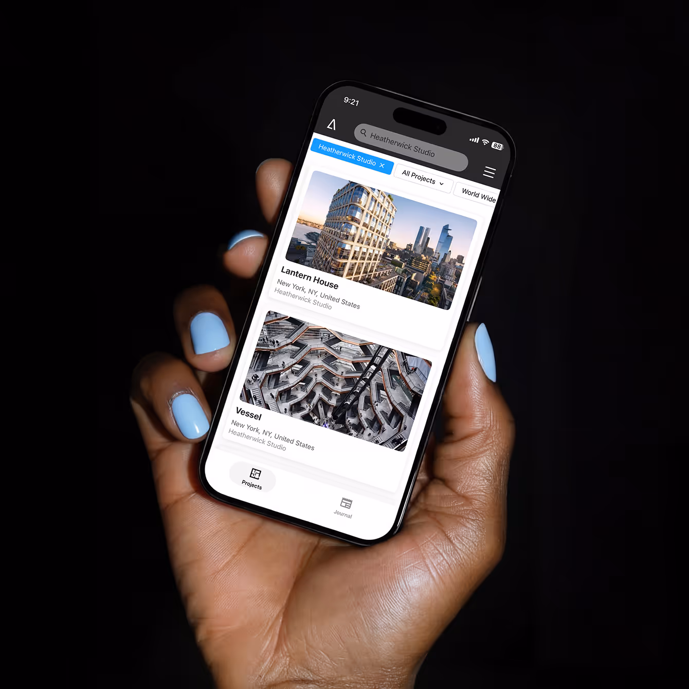 Hand with light blue nail polish holding a smartphone displaying architectural project listings for Lantern House and Vessel in New York by Heatherwick Studio.