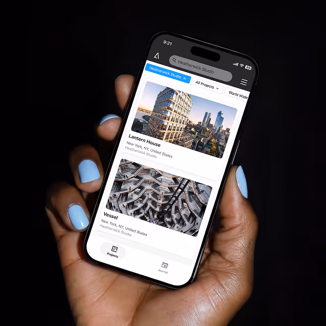 Hand with blue-painted nails holding a smartphone displaying architectural projects Lantern House and Vessel from Heatherwick Studio.