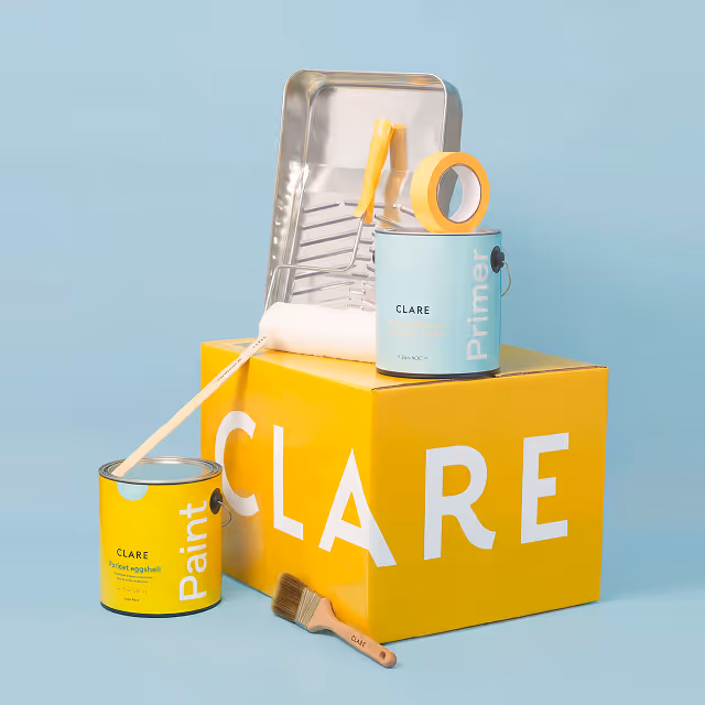 Yellow and light blue paint cans labeled 'CLARE' on and beside a yellow box with 'CLARE' text, with painting tools including a roller, paintbrush, paint tray, and masking tape.