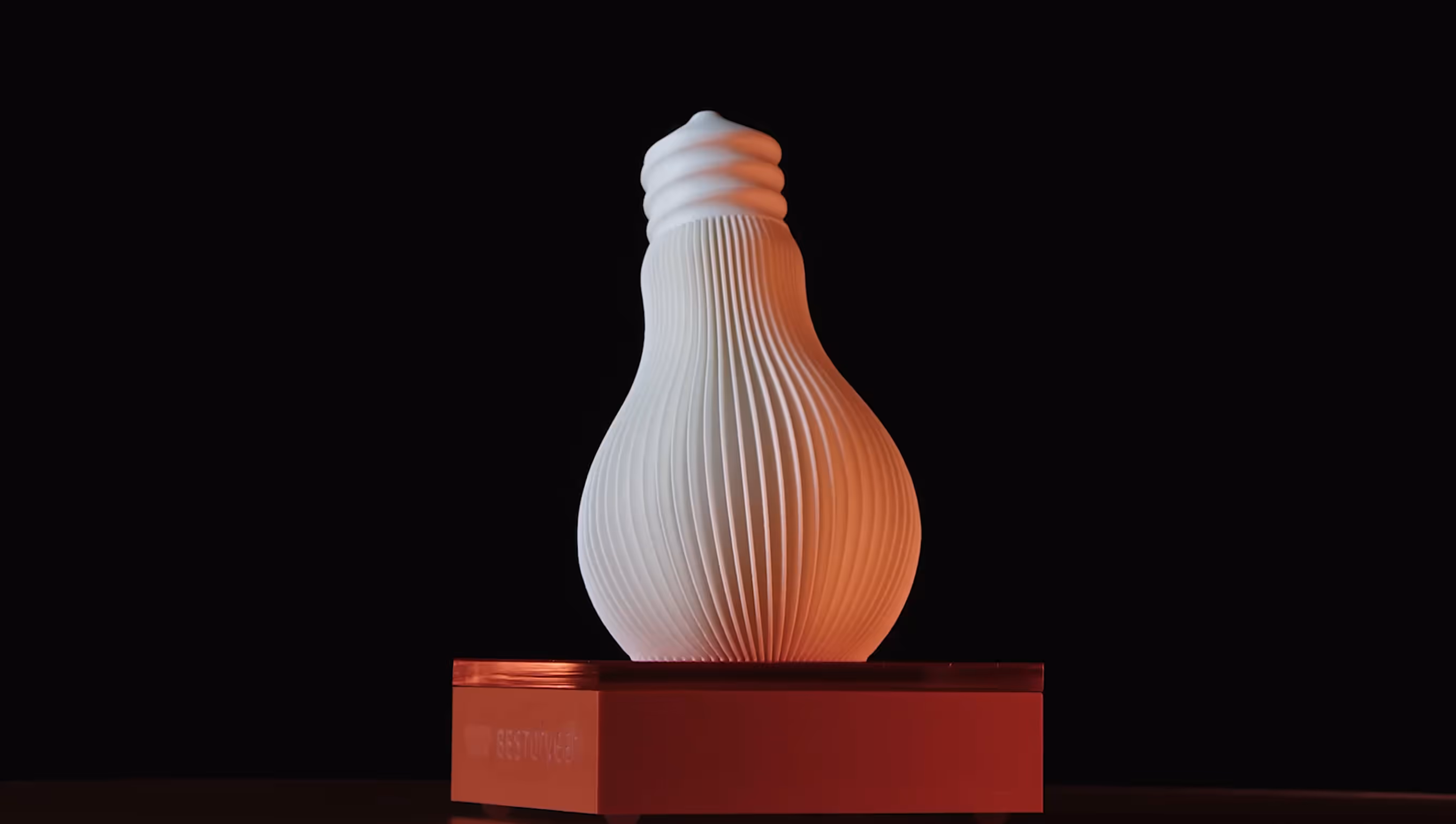 White 3D printed vase with vertical ridges on a red pedestal against a black background.