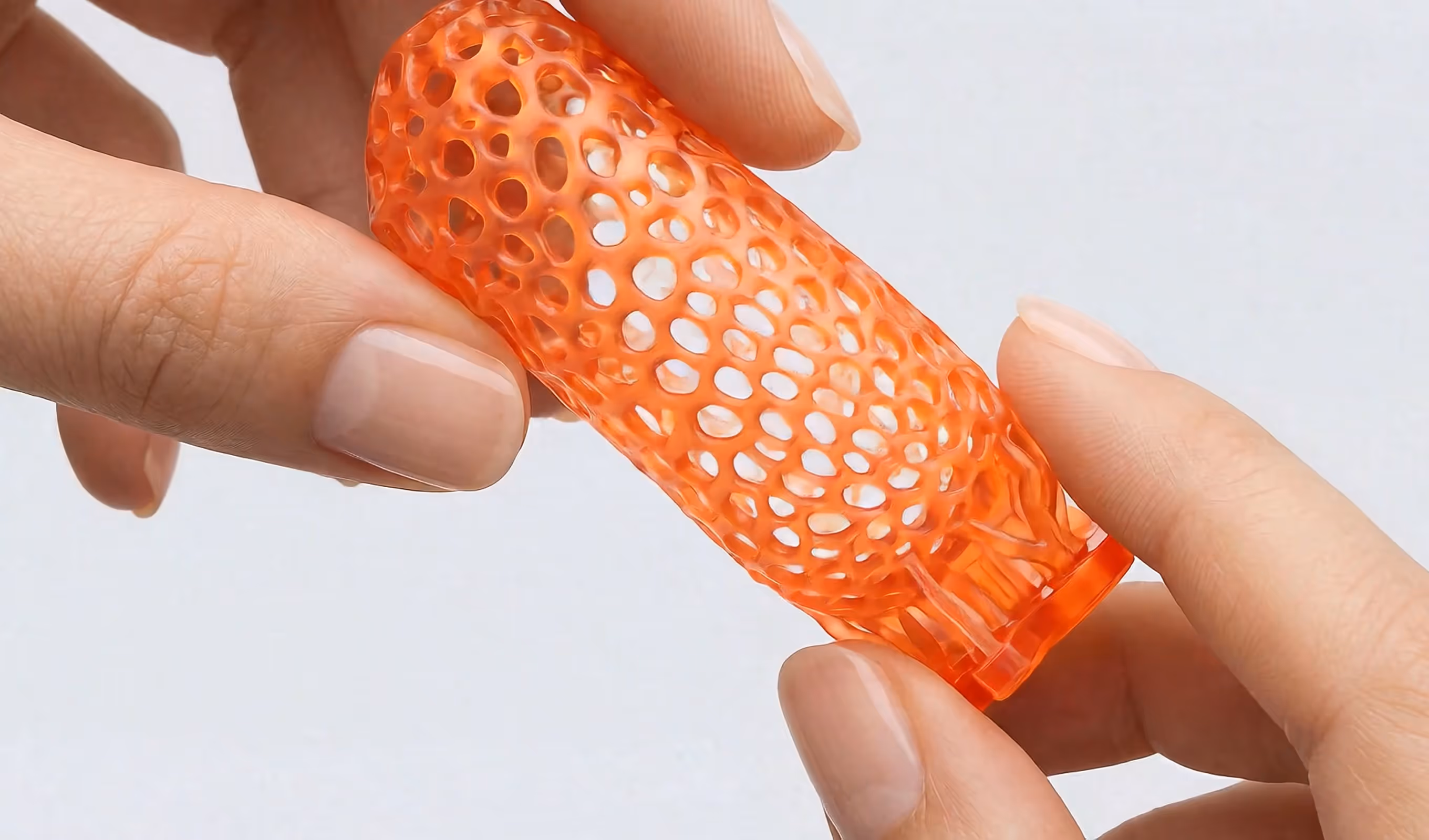 Close-up of hands holding an orange, lattice-structured, cylindrical object.