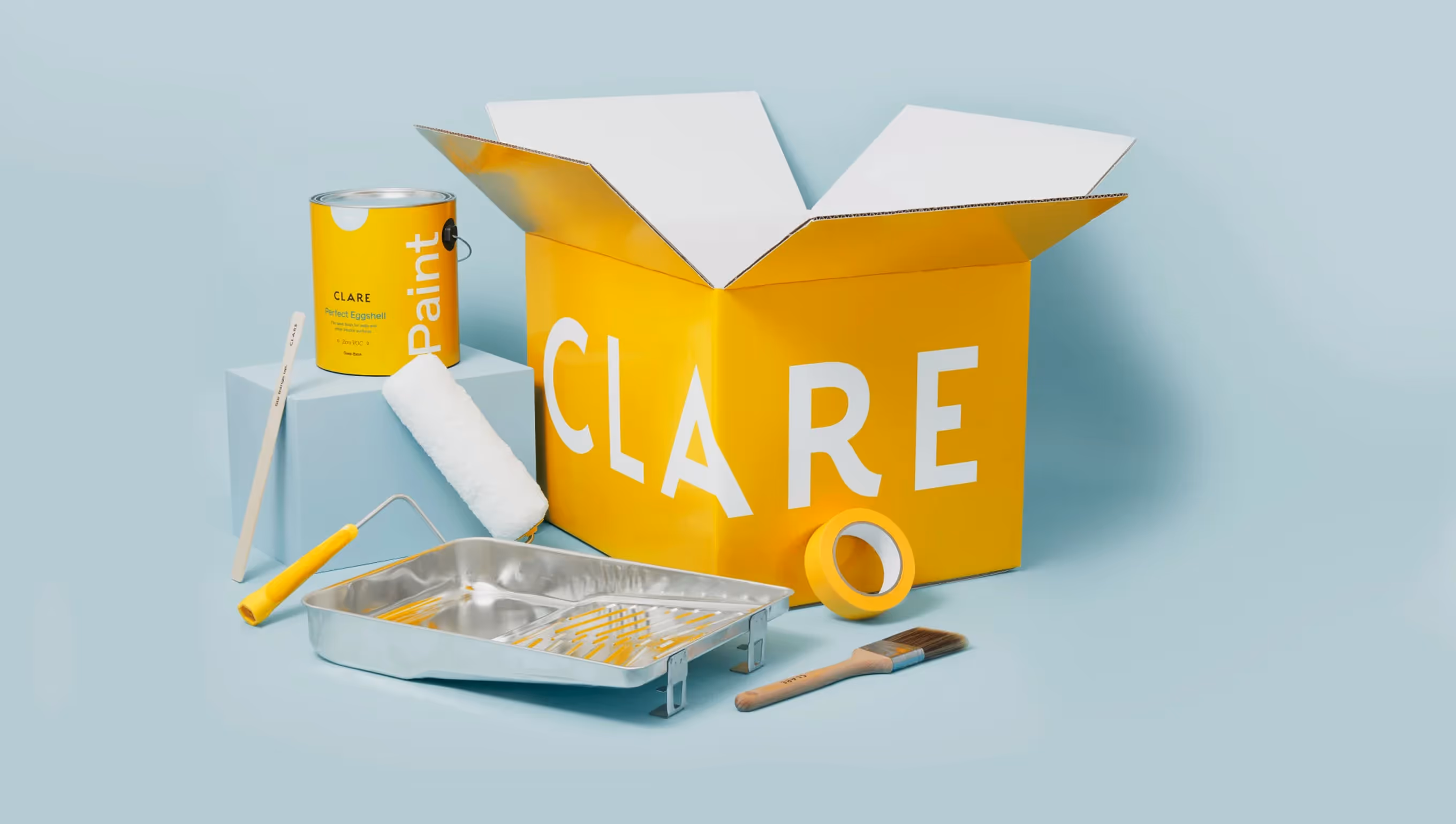 Yellow Clare paint can, paint roller, metal paint tray, paintbrush, tape, and a large yellow Clare box on a light blue background.