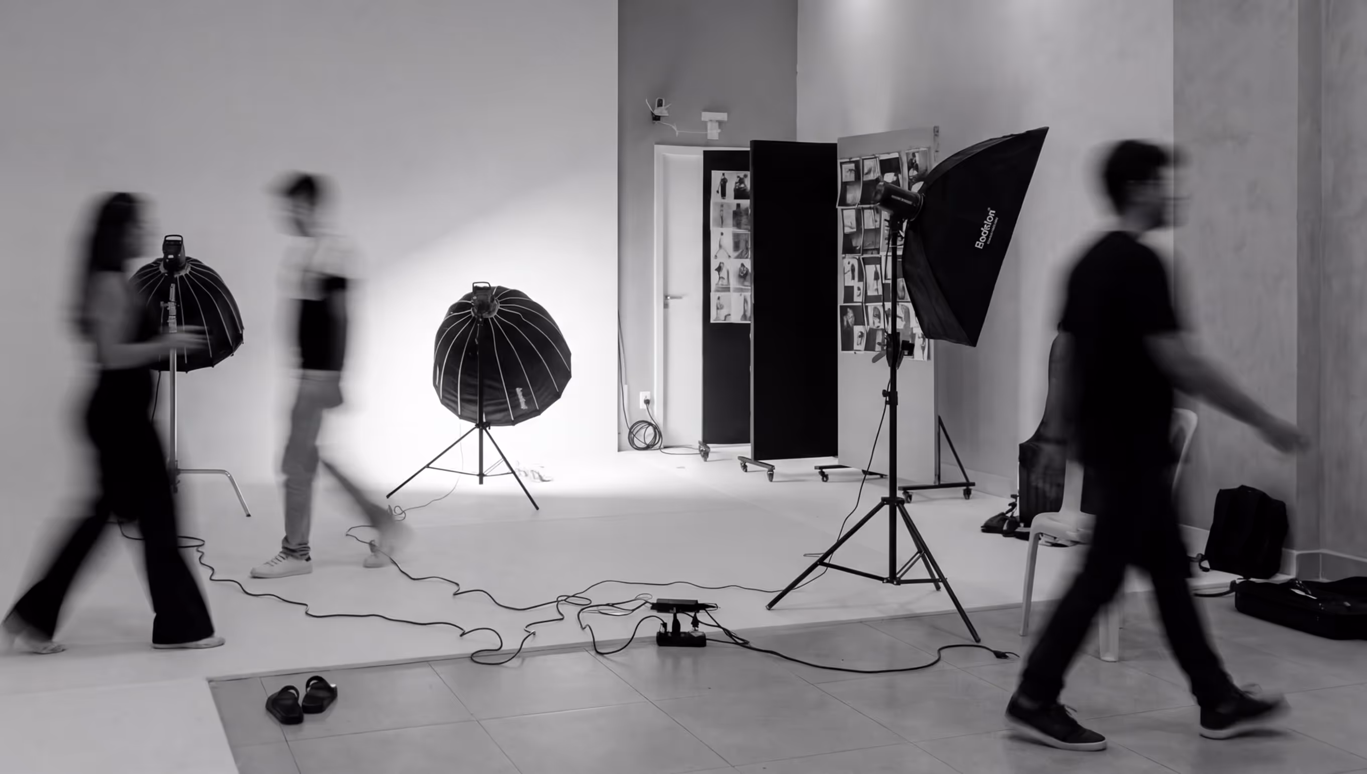 Black and white photo of a photography studio with softbox lights and three blurred people walking through.