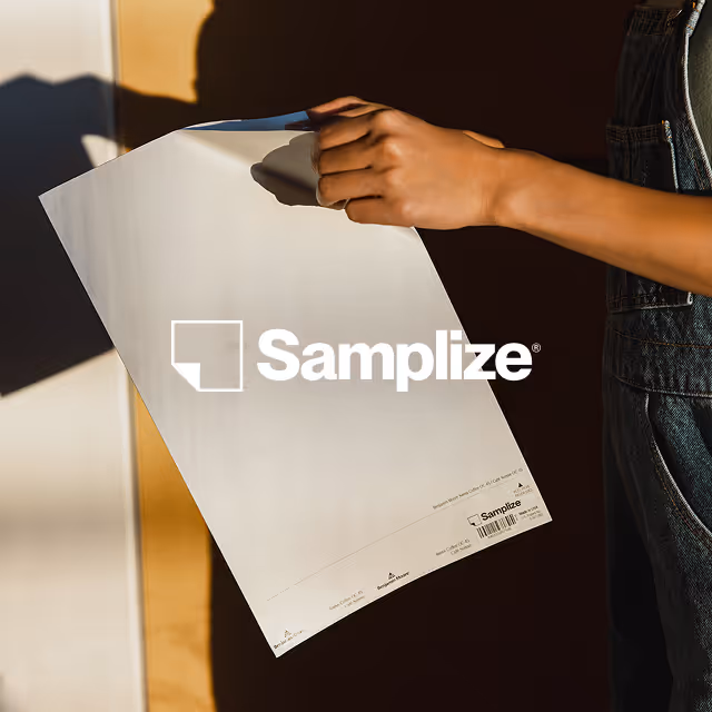 Person holding a white Sampleze branded paper sheet against a dark background.