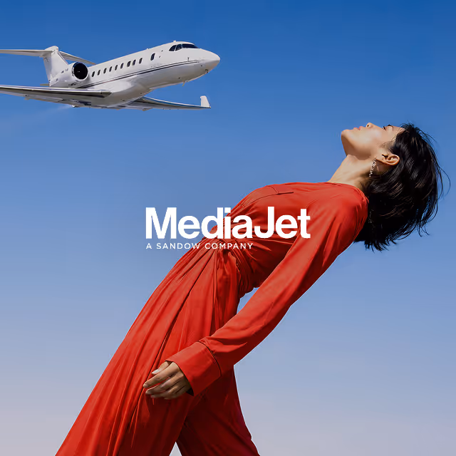 Woman in a flowing red dress leaning backward against a clear blue sky with a private jet flying above.