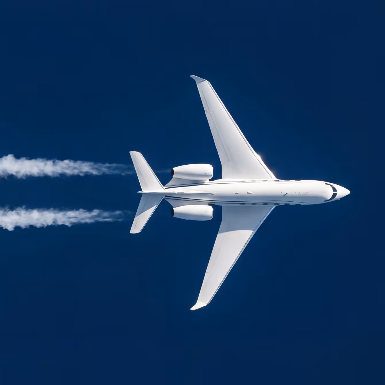 White jet airplane flying high in clear blue sky leaving two contrails behind.