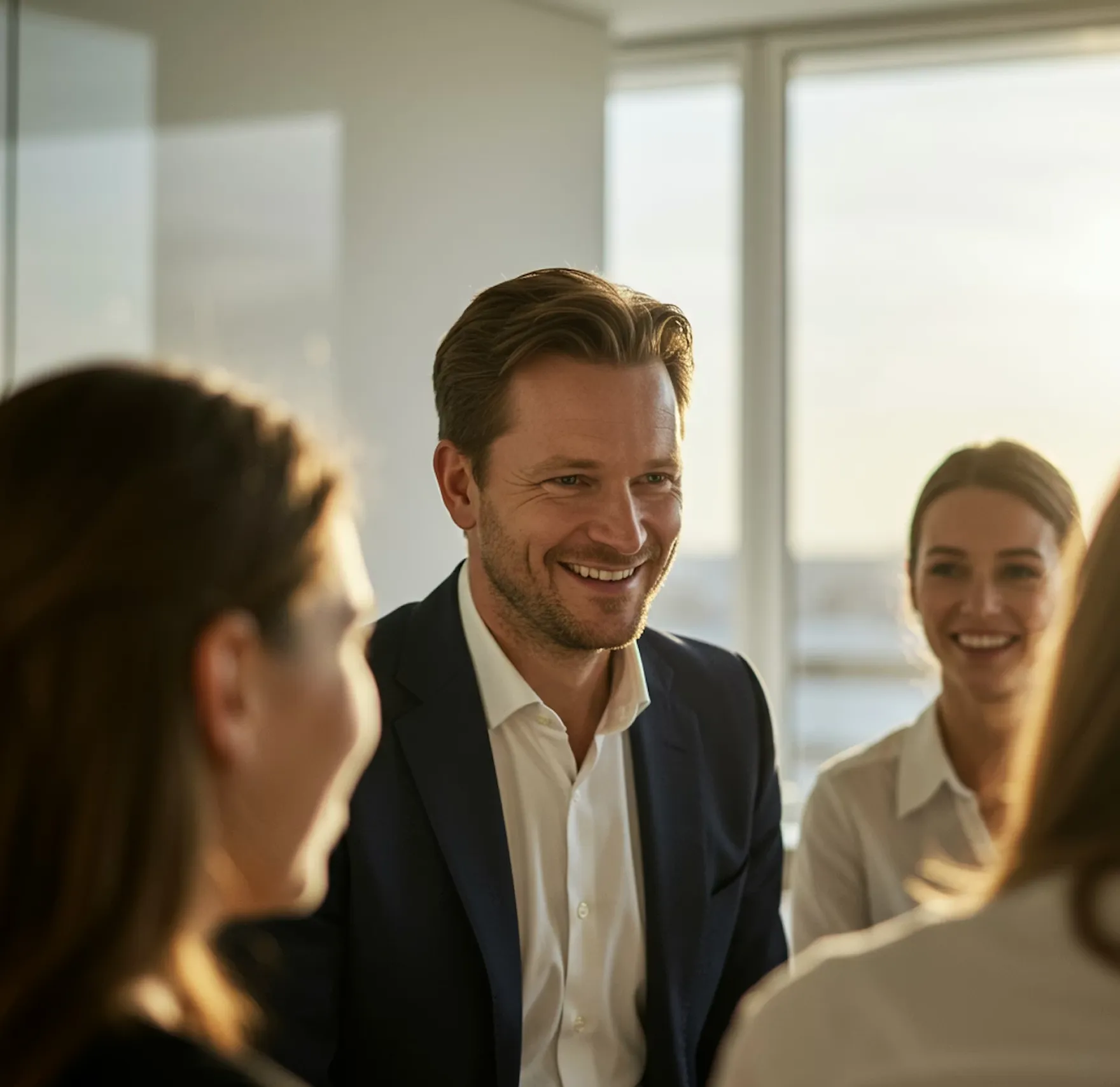 Smiling businessman in a dark suit engaging in conversation with colleagues in a bright office.