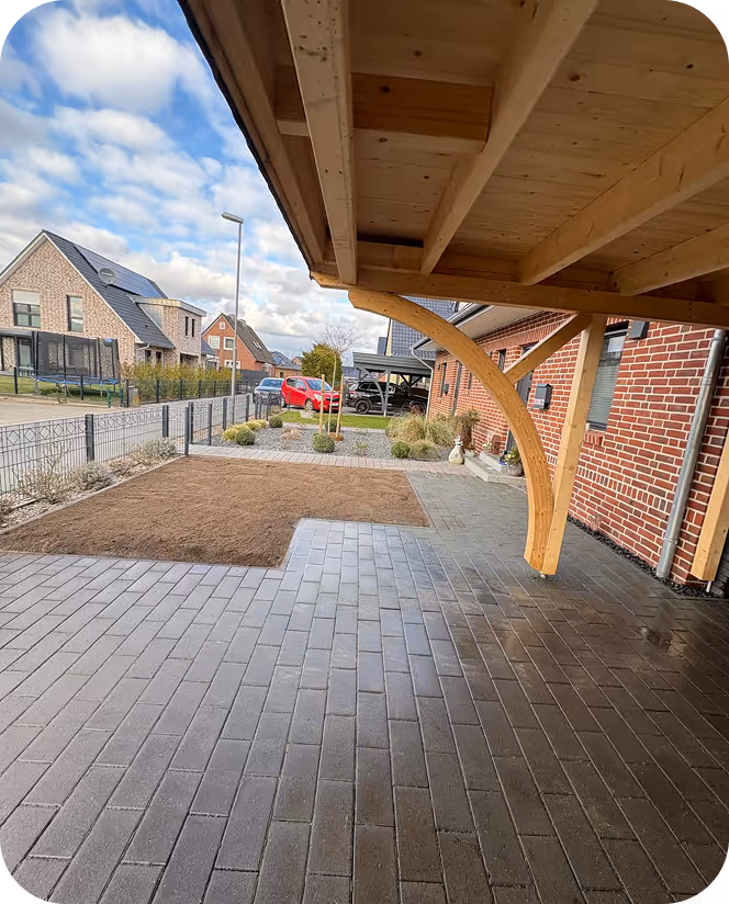 Überdachte Einfahrt mit gepflastertem Boden und kleinem Rasenbereich neben einem roten Backsteinhaus in einer Wohngegend.