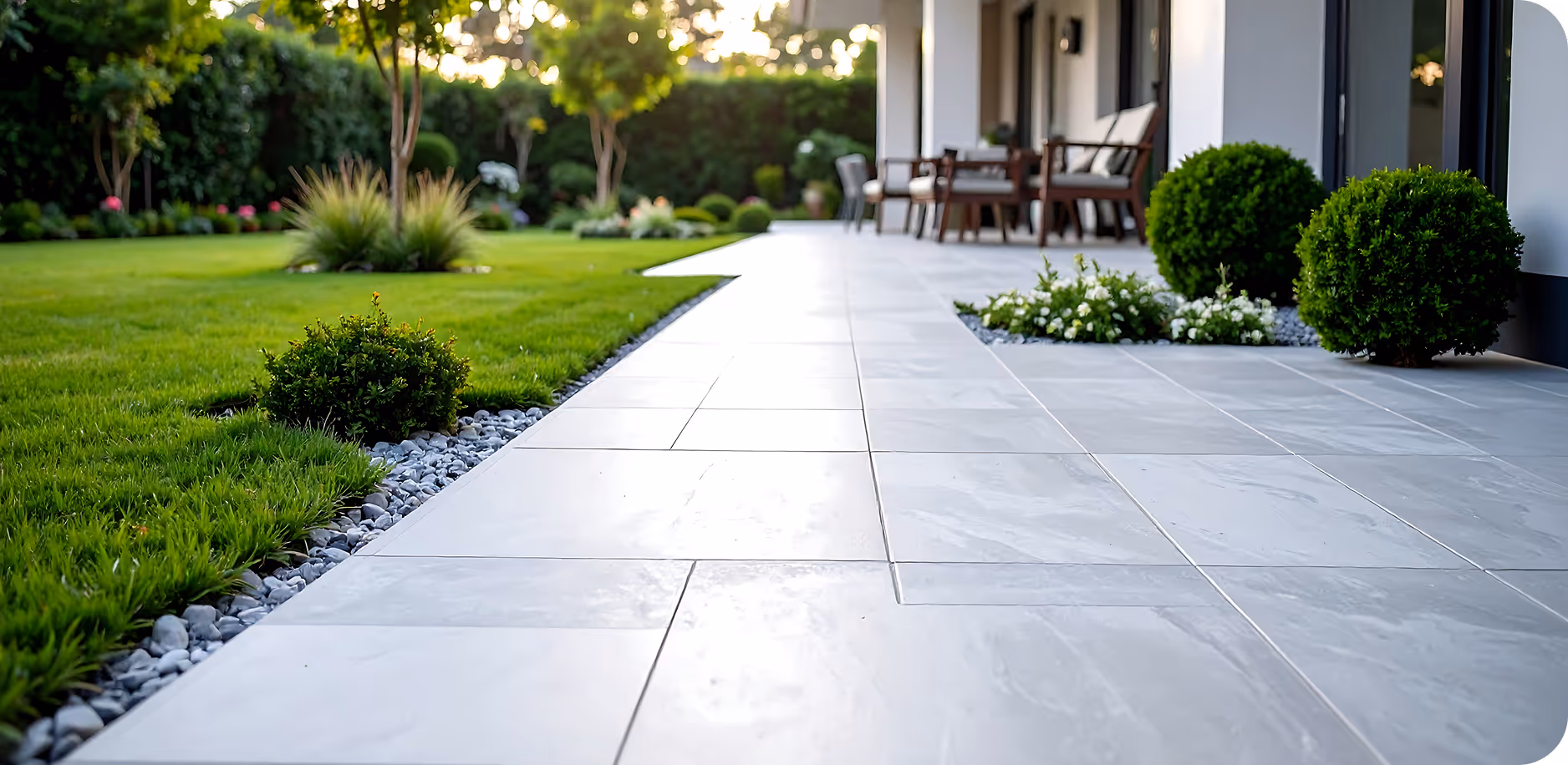 Moderne Terrasse mit grauen Steinplatten, gepflegtem Rasen und dekorativen Büschen an einem sonnigen Tag.