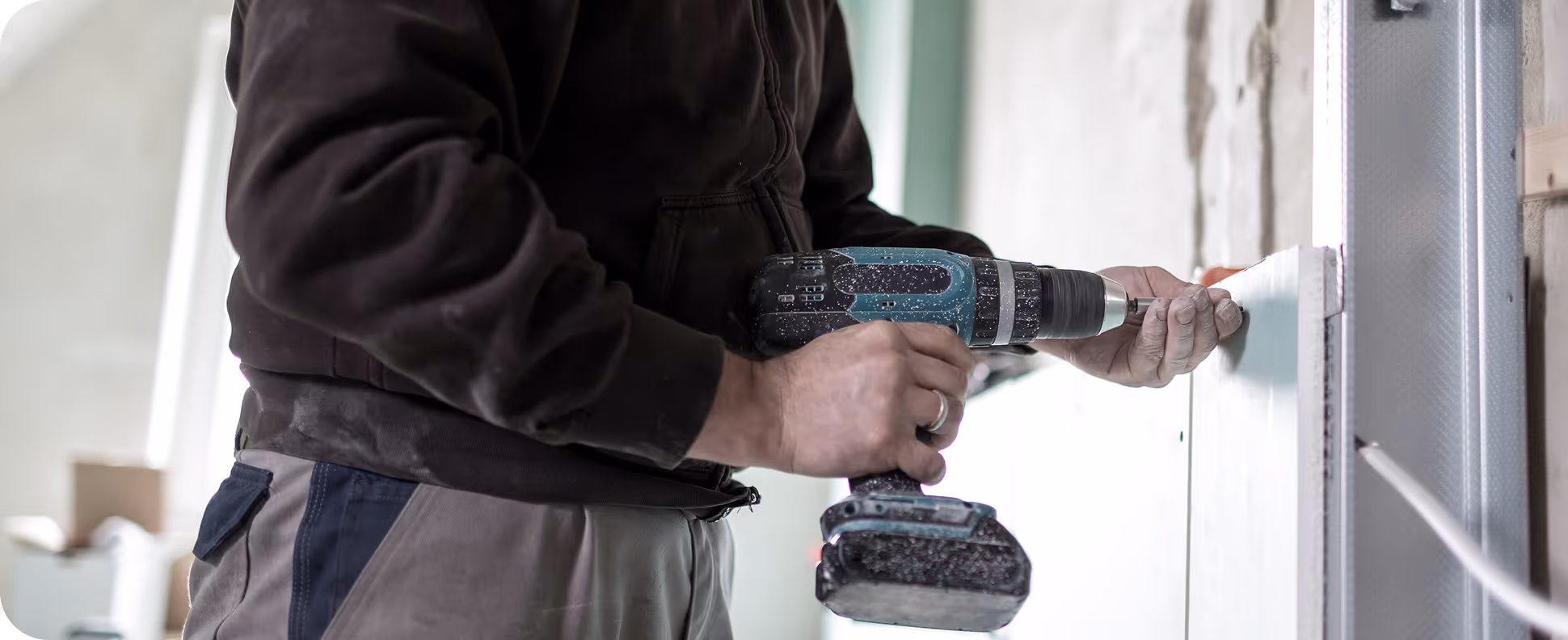 Handwerker befestigt mit einem Akku-Bohrschrauber ein weißes Paneel an einer Wand.