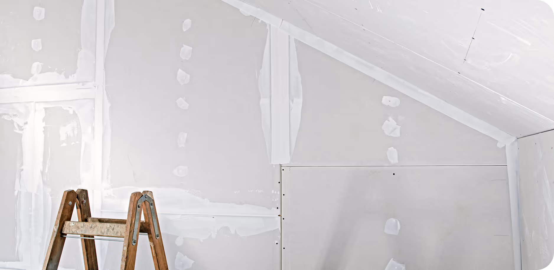 Unfertige Wand mit Trockenbauplatten und Spachtelmasse, davor eine Holzleiter.
