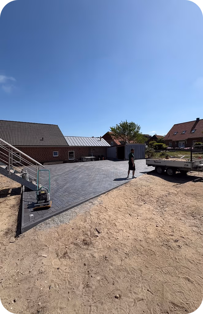 Ein Mann steht neben einer neu gepflasterten Einfahrt vor einem Haus an einem sonnigen Tag.