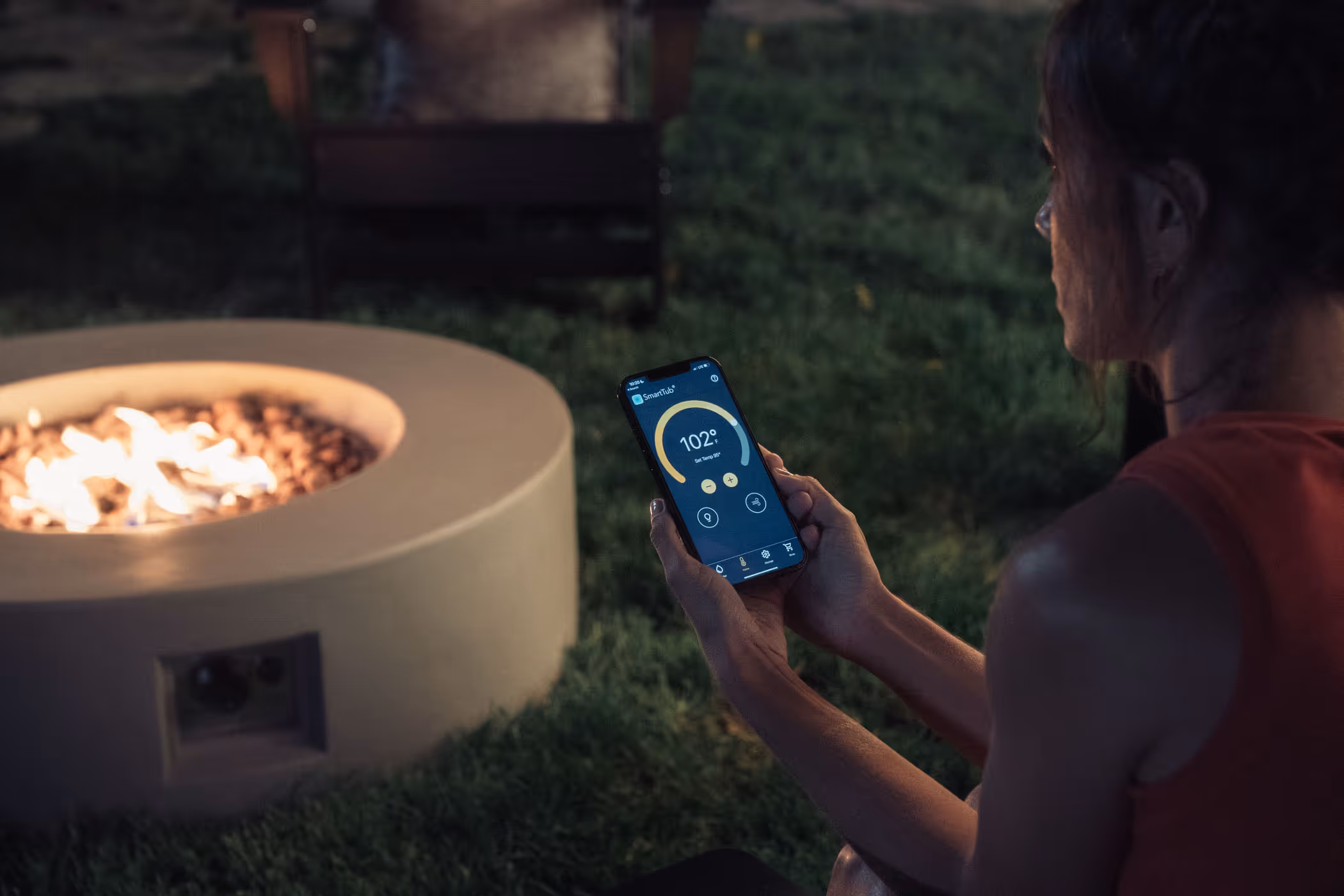 woman sitting next to a fire pit with her phone with smart tub
