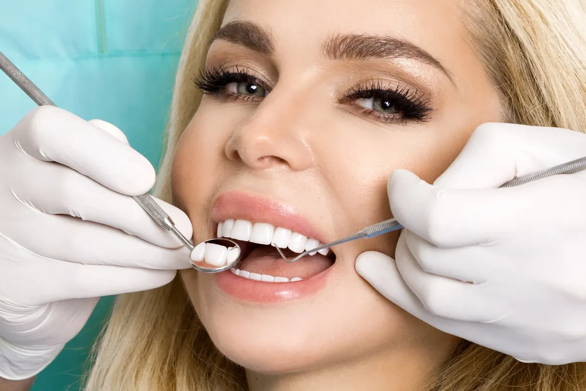 Dentist examining a smiling blonde woman’s teeth with dental mirror and probe.