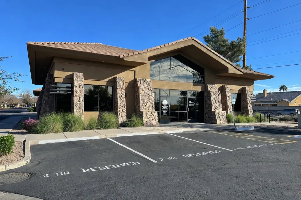 Single-story building with stone pillars and reserved 2-hour parking spaces in front under a clear blue sky.