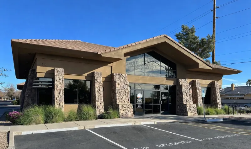 Office building with stone pillars, large windows, and adjacent parking spaces under clear blue sky.