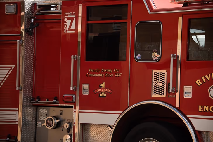 Close-up of a red fire truck door with text 'Proudly Serving Our Community Since 1887' and various firefighting equipment details.
