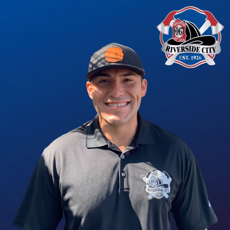 Smiling man wearing a black cap and black Riverside City firefighter polo shirt against a blue background with Riverside City firefighter emblem.