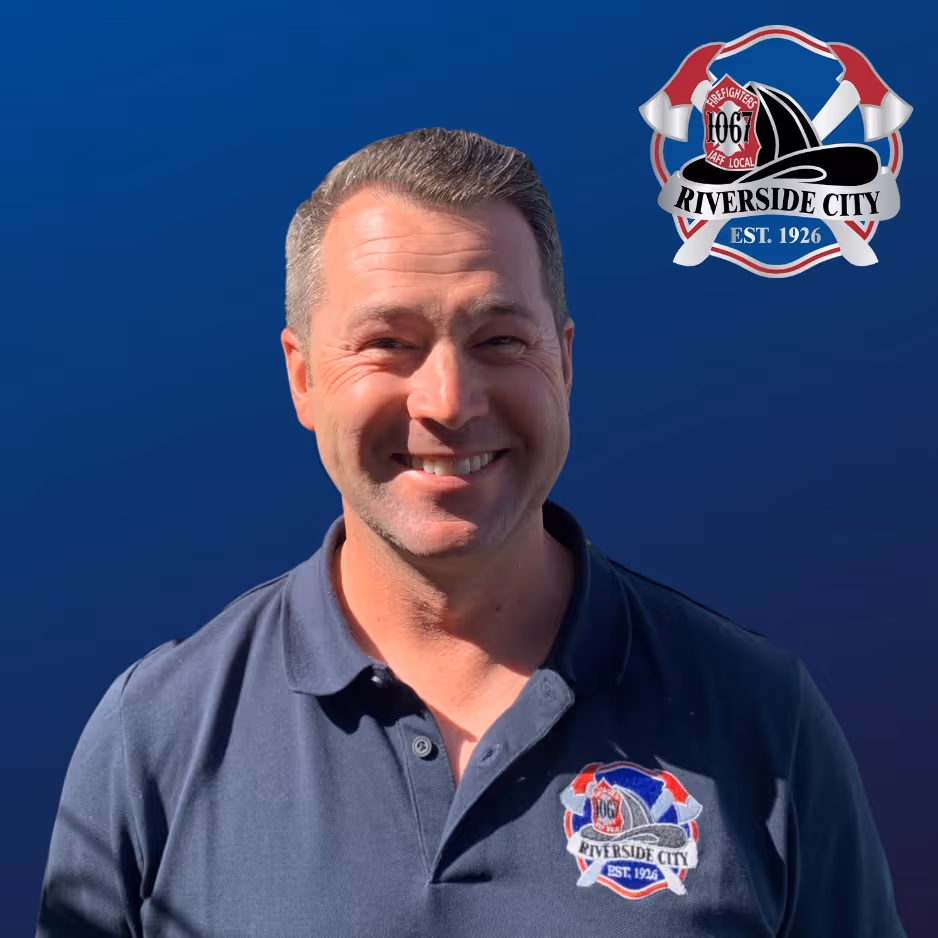 Smiling man wearing a navy blue polo shirt with Riverside City Firefighters Local 1067 logo on chest, standing in front of a blue background with the same logo.
