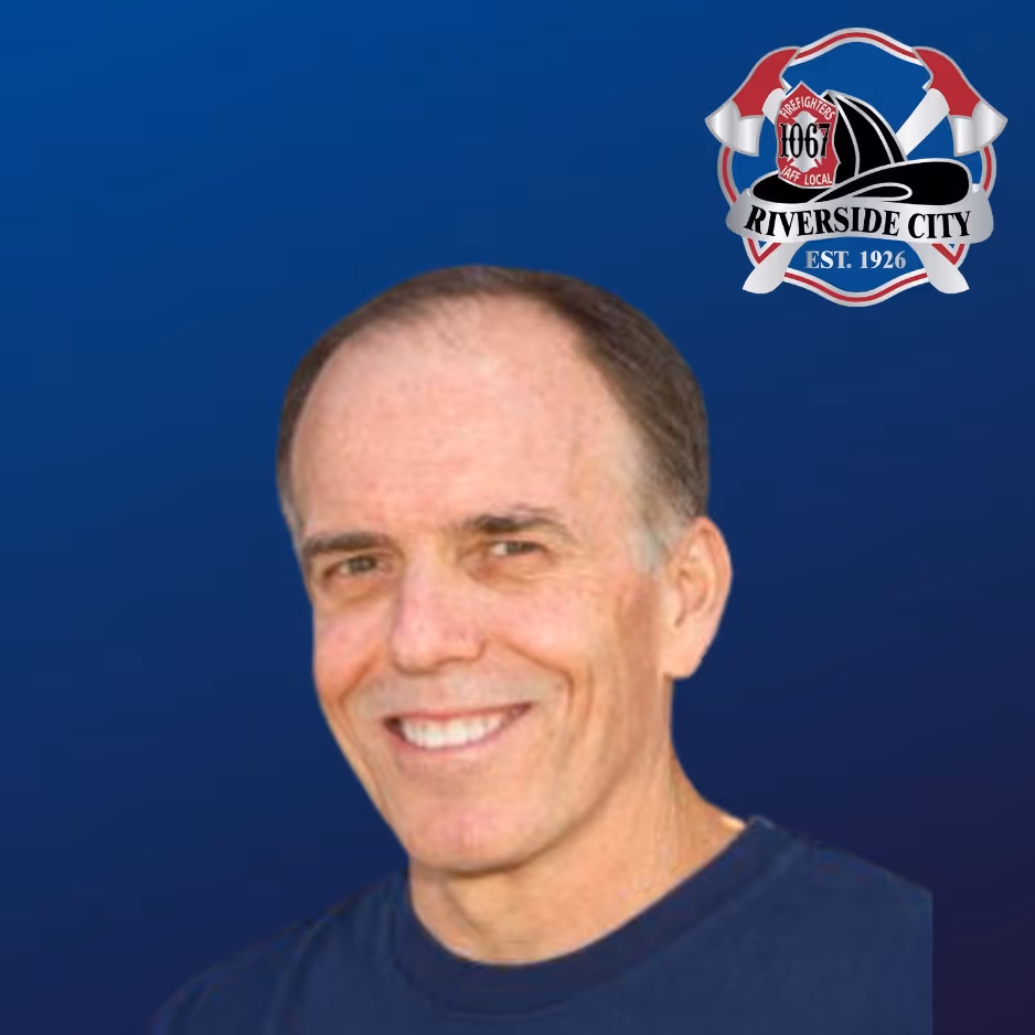 Smiling middle-aged man with short hair wearing a dark blue shirt against a blue background with the Riverside City Firefighters Local 1067 logo.