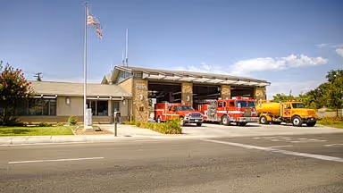 Fire station with several fire trucks and an American flag on a flagpole outside.