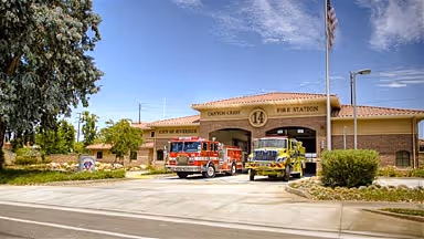 Canyon Crest Fire Station 14 with two fire trucks parked outside under a partly cloudy sky.