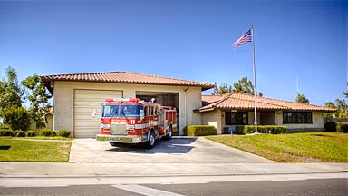 Red fire truck parked in front of a single-story fire station with an American flag on a flagpole.