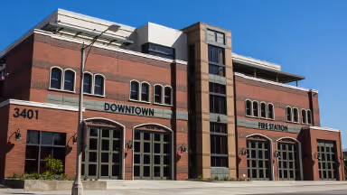 Brick downtown fire station building with large garage doors and a clear blue sky.