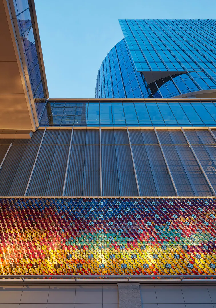 Low-angle view of modern glass buildings with a colorful reflective mosaic panel on the facade.