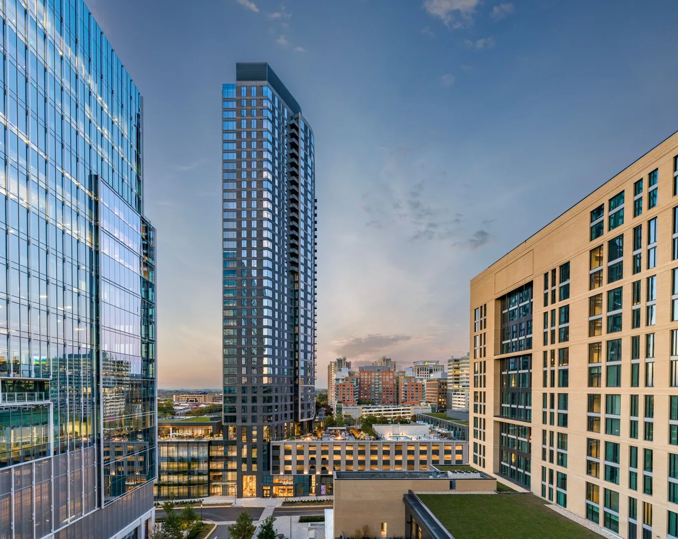 Modern cityscape with high-rise glass and brick buildings at dusk under a partly cloudy sky.