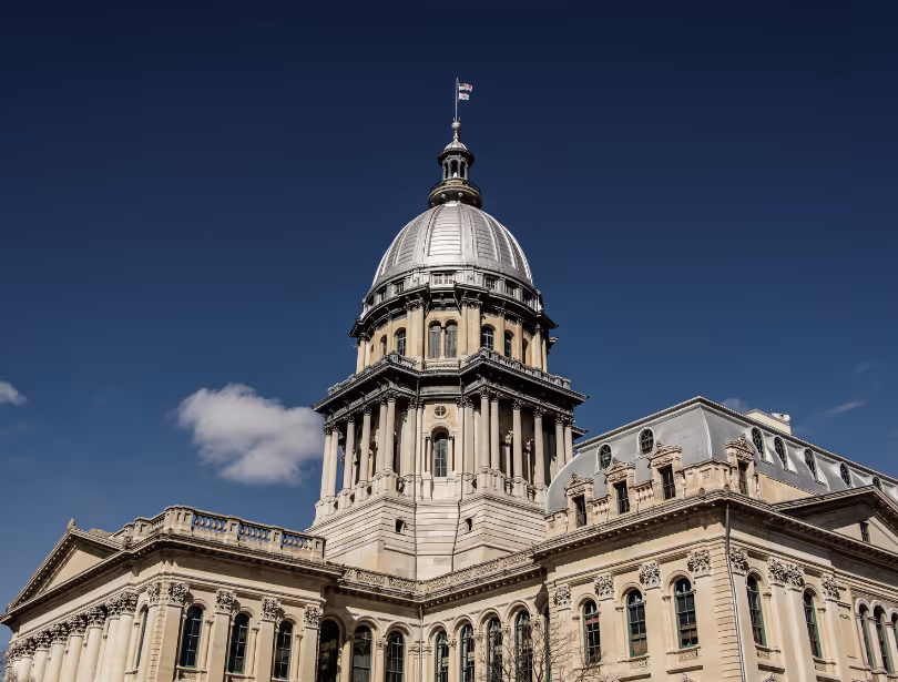 The Illinois State Capitol building with its prominent dome under a clear blue sky.