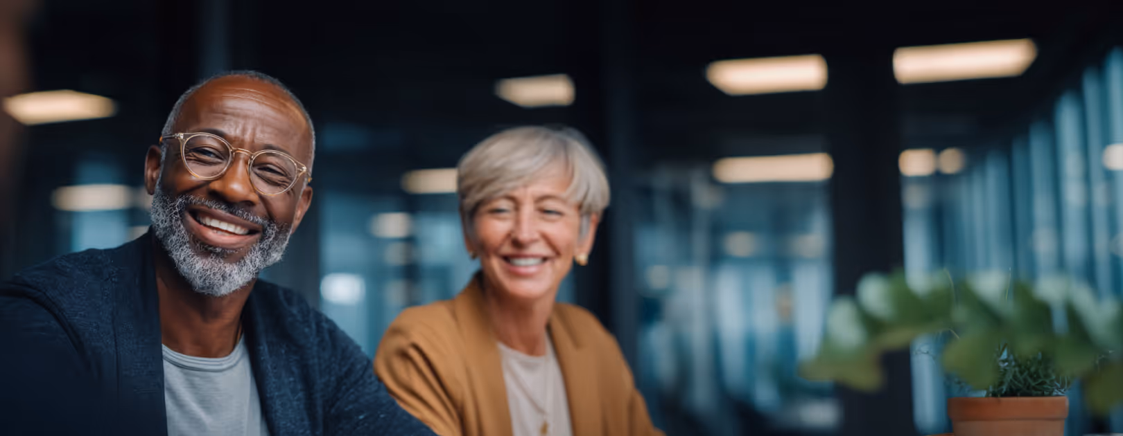 Smiling elderly man and woman sitting together in a modern office setting.