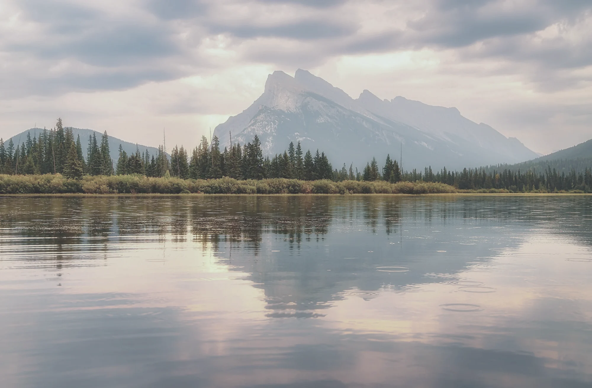 Mountain peak and evergreen shoreline reflected in a still lake under soft clouds