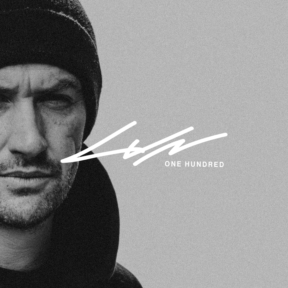 Black and white close-up of a man wearing a beanie and a hoodie, with a white stylized signature and the text "ONE HUNDRED" on the right side.