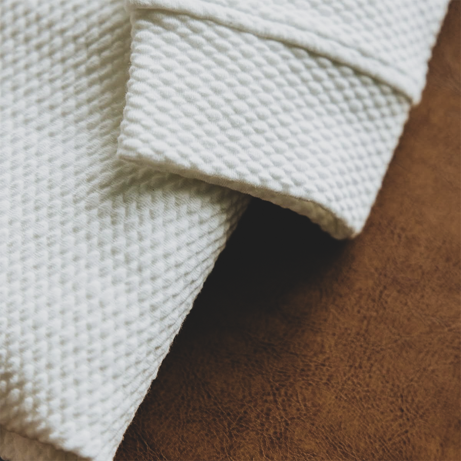 Close-up of folded white textured fabric on a brown leather surface.