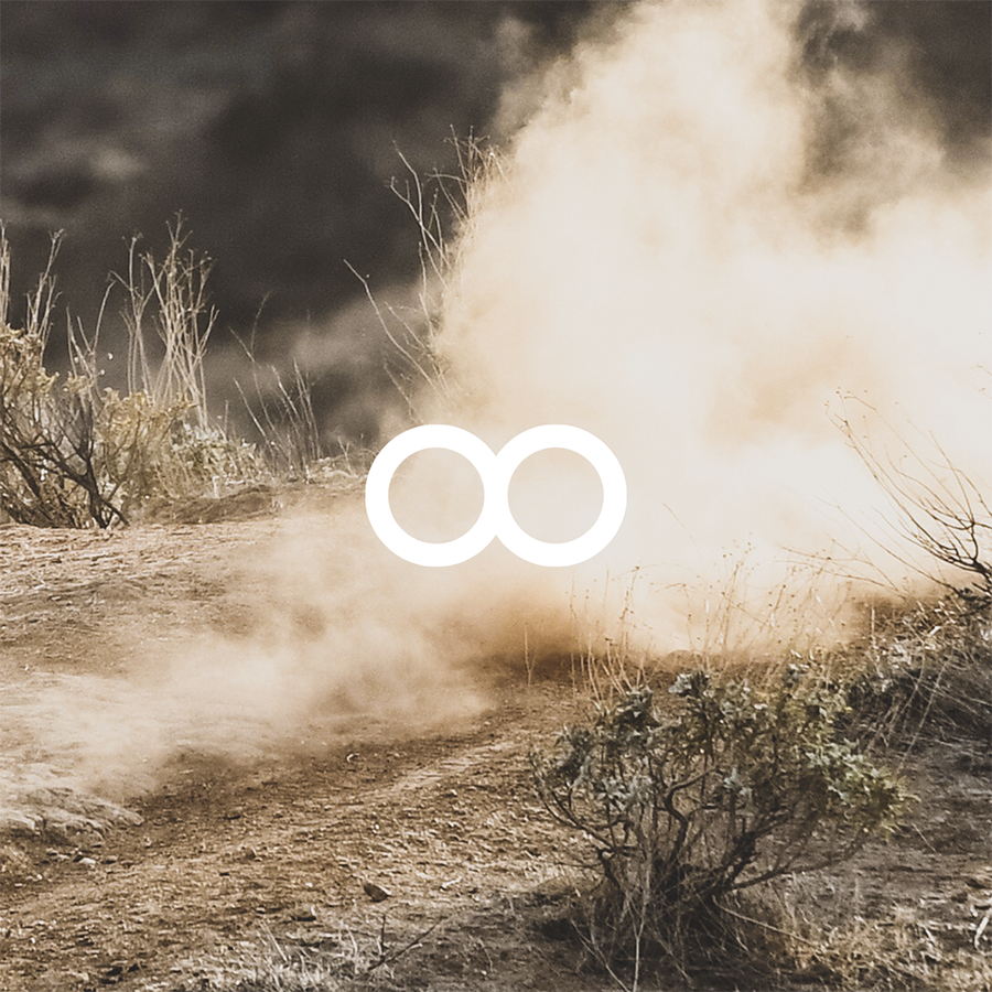 Dust cloud rising on a dry dirt trail surrounded by sparse shrubs.