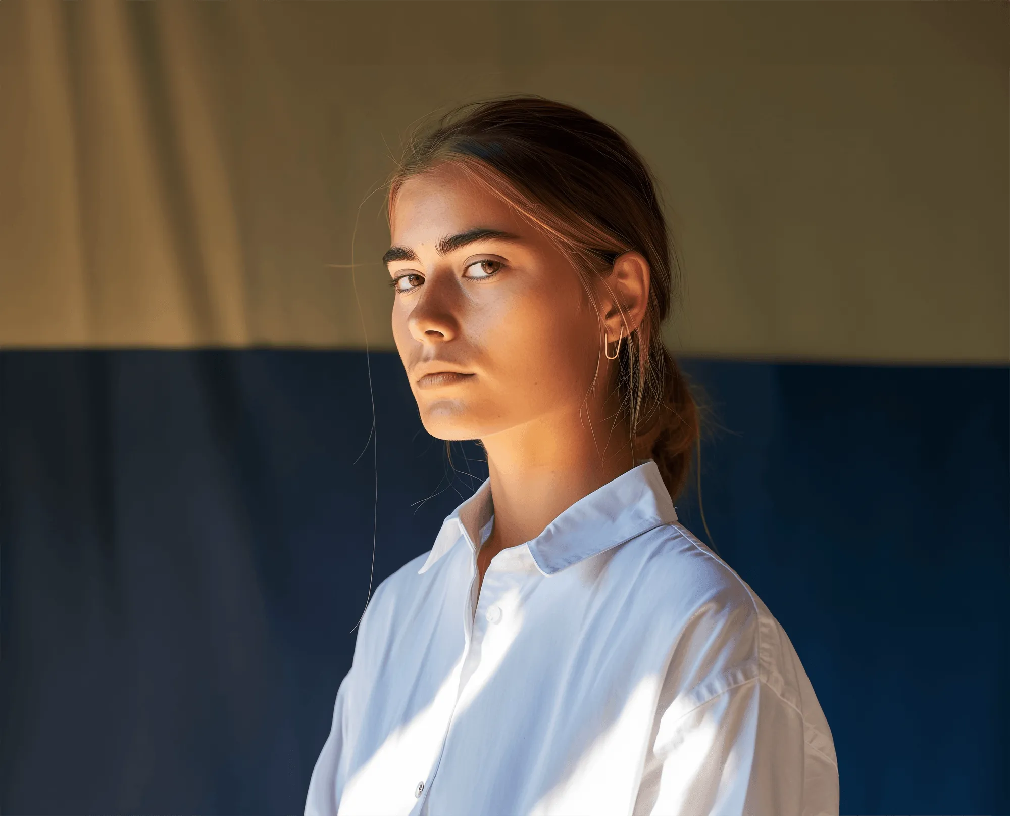 Jeune femme sérieuse portant une chemise blanche avec un fond bicolore bleu et beige.