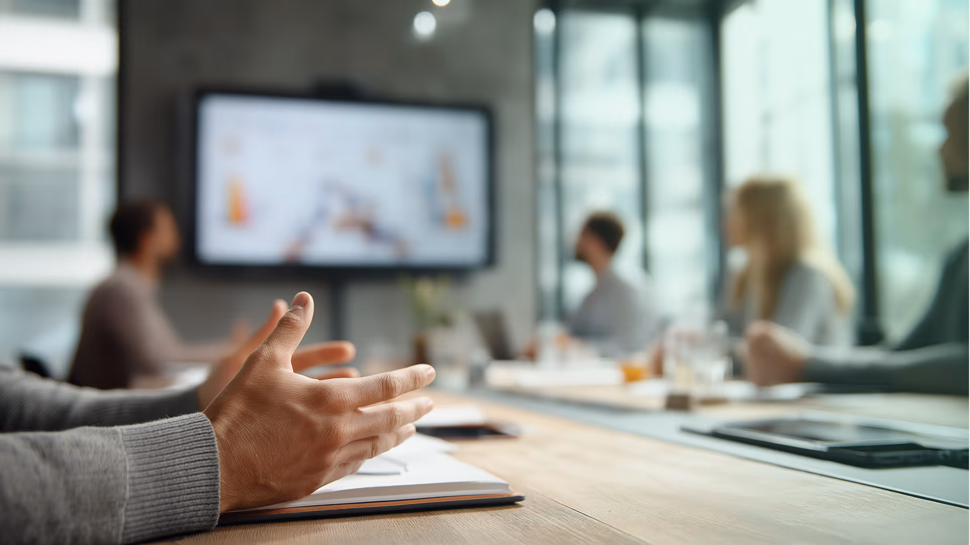Des mains en mouvement lors d'une réunion d'équipe avec un écran de présentation en arrière-plan flou. Présentation devant des acteurs du secteur de la formation et EdTech.