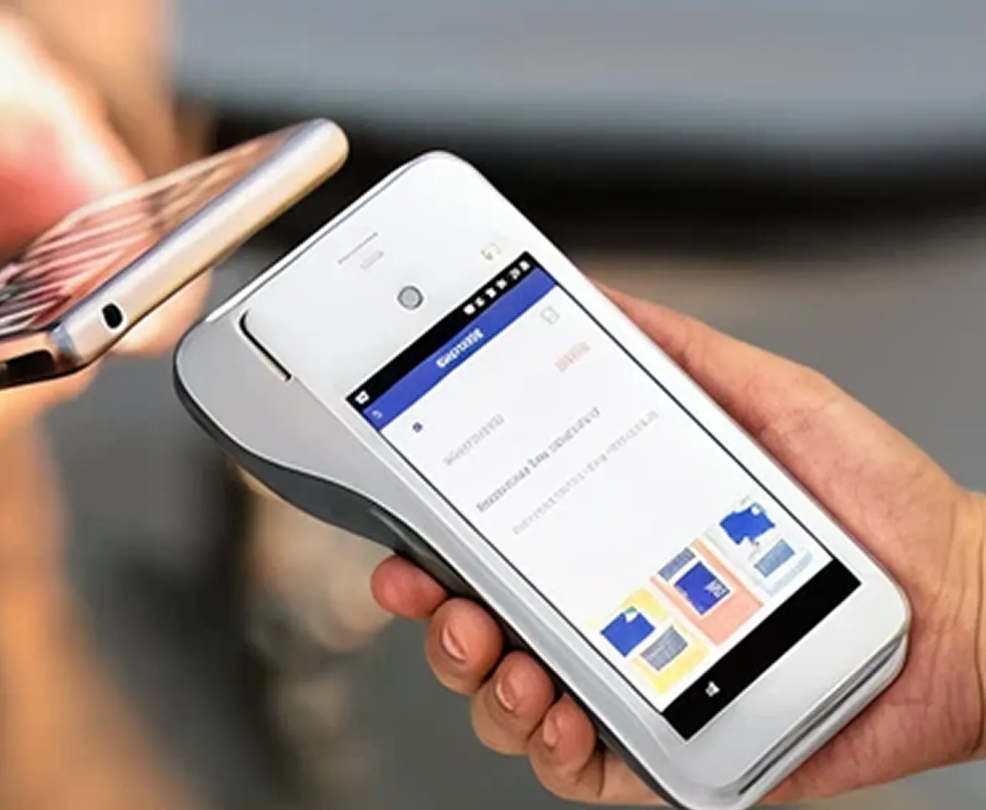 Hand holding a white mobile card reader with a smartphone tapping to make a payment.
