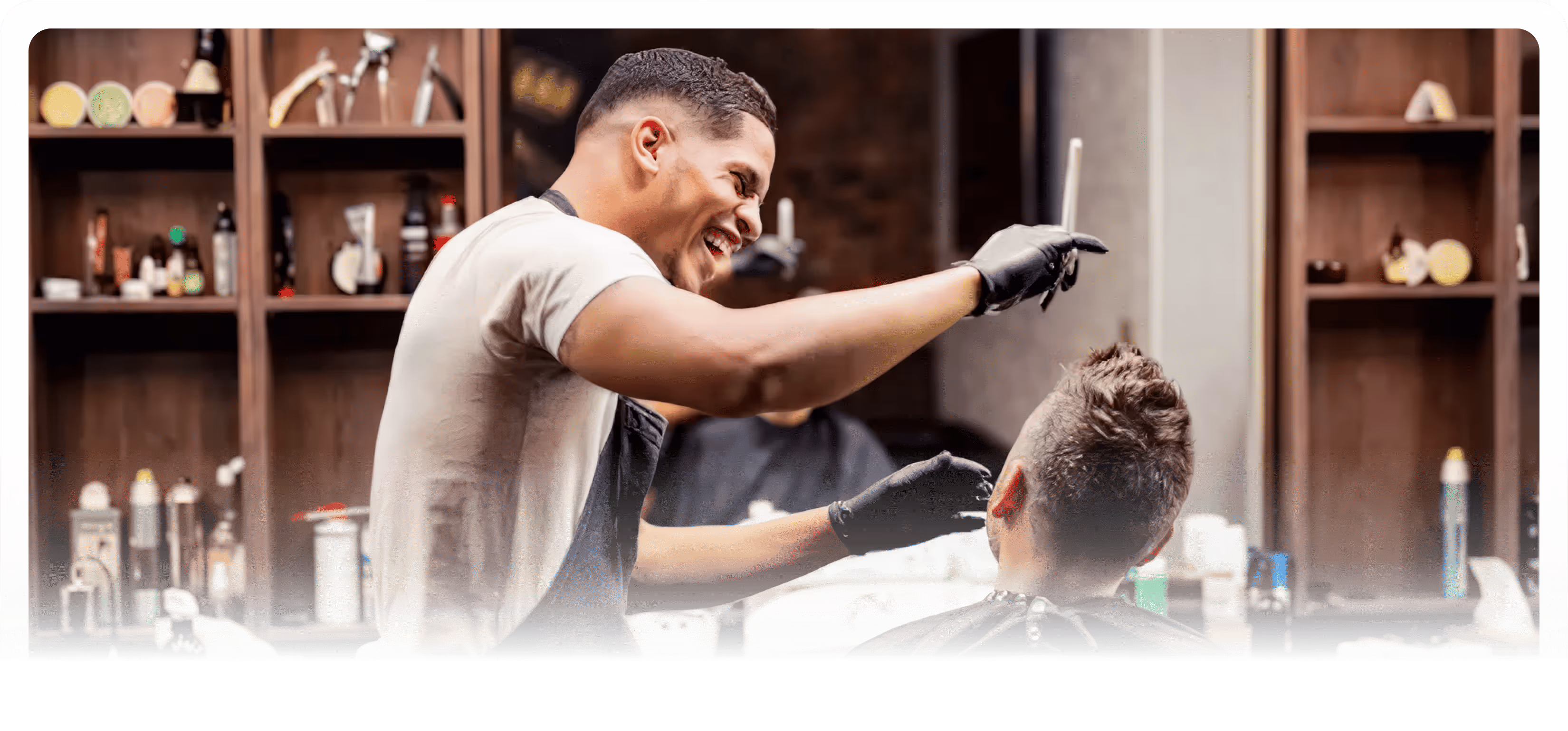 Smiling barber wearing black gloves styling a client's hair in a barbershop.