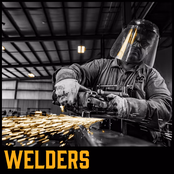 Welder in protective gear using a grinding tool, sparks flying in a workshop.