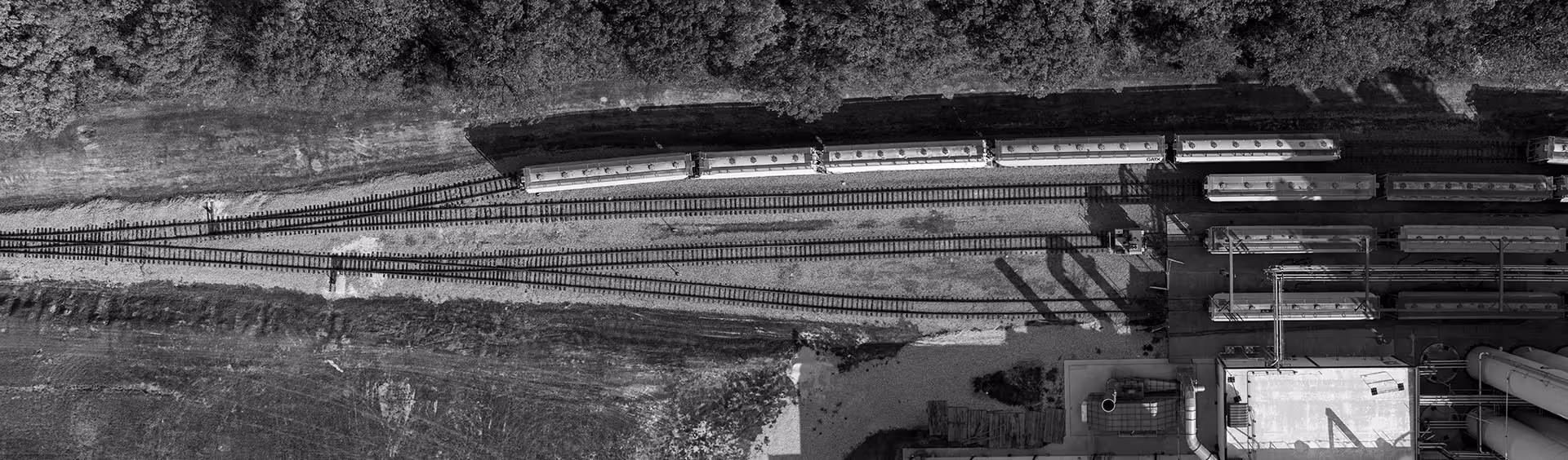 Aerial black and white view of multiple rail tracks converging near industrial buildings with parked train cars.