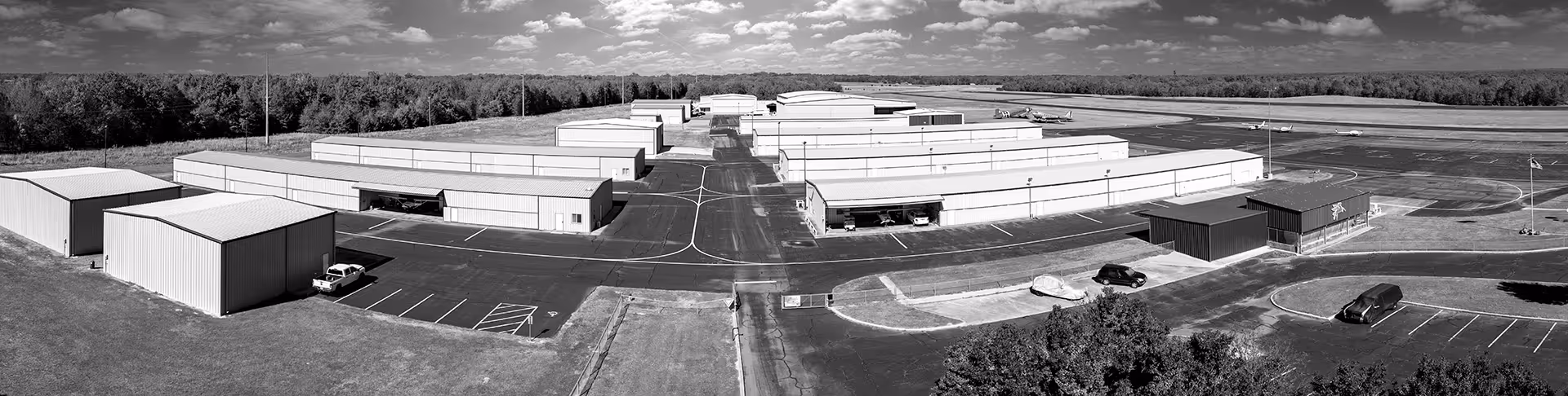 Aerial view of an airport with multiple airplane hangars, parked vehicles, and small planes on the runway.